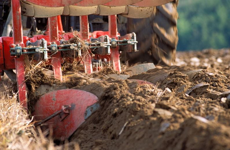 A red tractor turning dirt on a farm